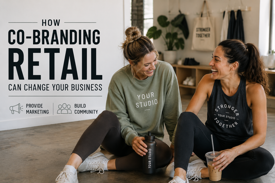 Two fitness studio members sitting together after class, laughing while wearing matching co-branded activewear in a bright boutique fitness studio, illustrating how branded apparel builds community and promotes a studio brand.